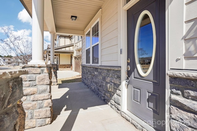 doorway to property featuring a porch and stone siding