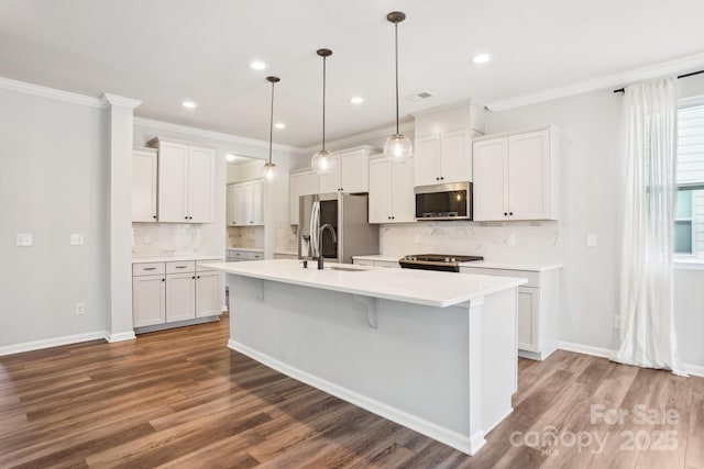 kitchen with light countertops, hanging light fixtures, appliances with stainless steel finishes, white cabinetry, and an island with sink