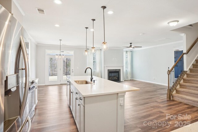 kitchen with stainless steel appliances, a sink, open floor plan, light countertops, and a center island with sink