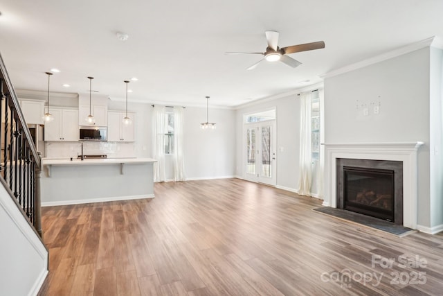 unfurnished living room featuring wood finished floors, baseboards, ornamental molding, stairway, and a glass covered fireplace