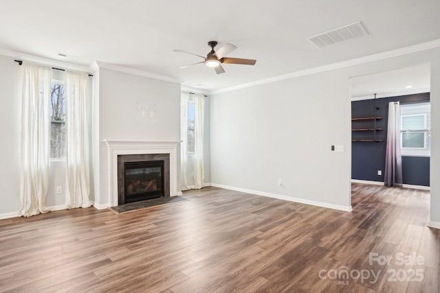 unfurnished living room featuring crown molding, visible vents, a glass covered fireplace, wood finished floors, and baseboards