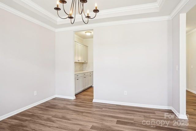 unfurnished dining area featuring crown molding, baseboards, a notable chandelier, and wood finished floors