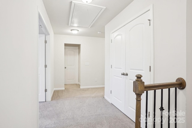 hall featuring baseboards, attic access, and light colored carpet