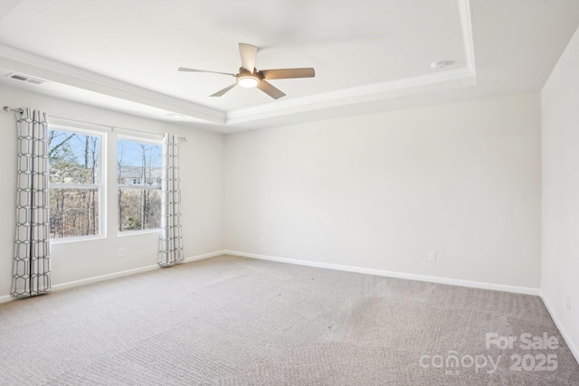 carpeted spare room with baseboards, visible vents, a raised ceiling, and a ceiling fan