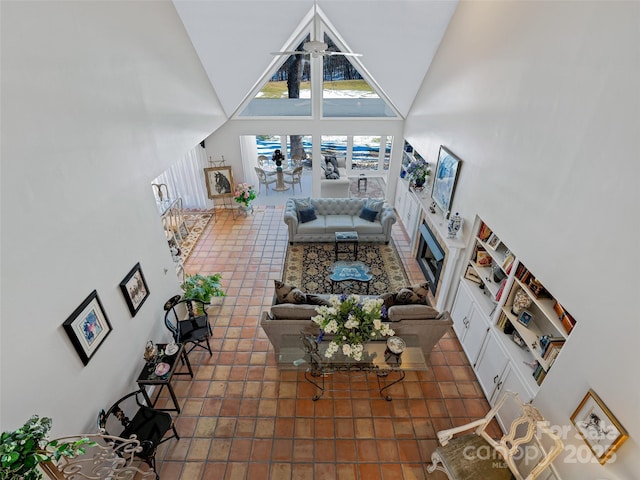 unfurnished living room featuring ceiling fan, dark tile patterned flooring, high vaulted ceiling, and a tile fireplace