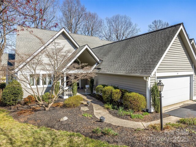 view of front of home featuring driveway, covered porch, a garage, and roof with shingles