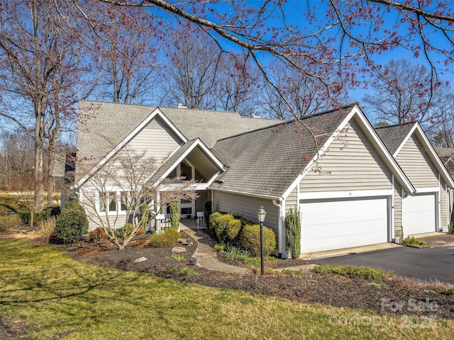 view of front of home featuring covered porch, a garage, a shingled roof, and a front yard