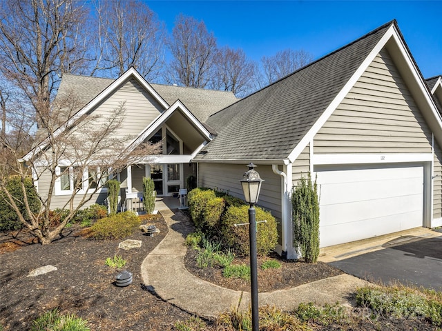 view of front facade featuring a shingled roof, covered porch, a garage, and aphalt driveway