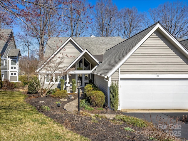 view of front of home featuring a front lawn, an attached garage, and roof with shingles