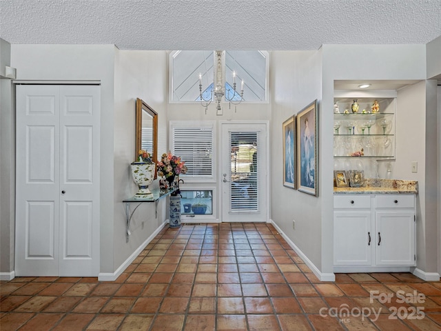 foyer with baseboards, a textured ceiling, tile patterned floors, and a notable chandelier