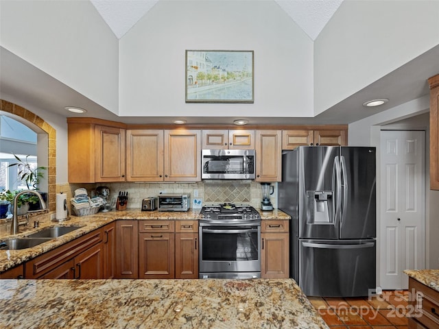 kitchen featuring high vaulted ceiling, a sink, light stone counters, and appliances with stainless steel finishes