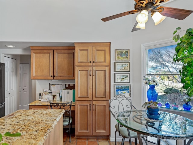 kitchen featuring a ceiling fan, light stone countertops, and brown cabinets