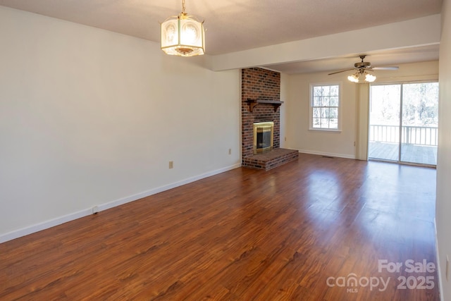 unfurnished living room with baseboards, a brick fireplace, dark wood finished floors, and ceiling fan with notable chandelier