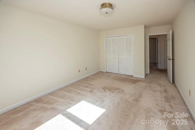 unfurnished bedroom with baseboards, a closet, and light carpet