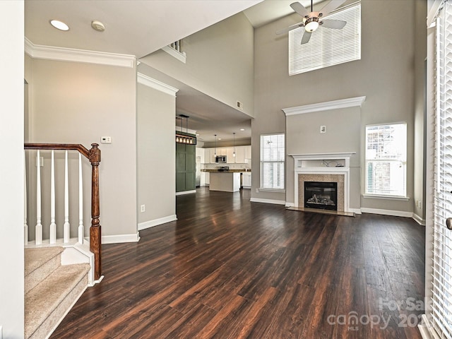 unfurnished living room featuring ceiling fan, a premium fireplace, dark hardwood / wood-style flooring, and a wealth of natural light