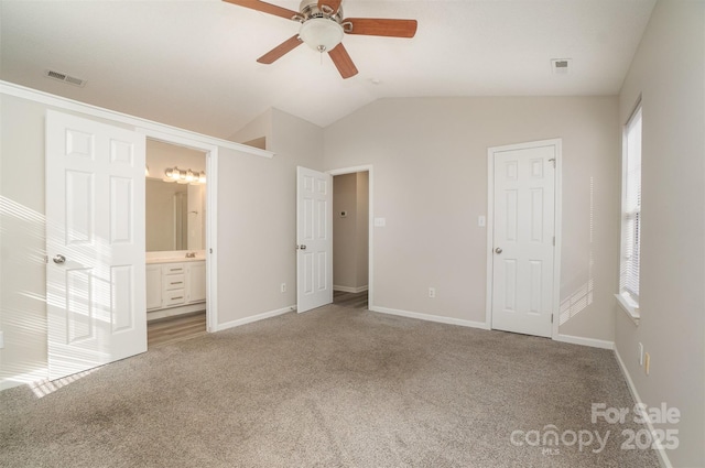 unfurnished bedroom featuring lofted ceiling, connected bathroom, multiple windows, and carpet flooring