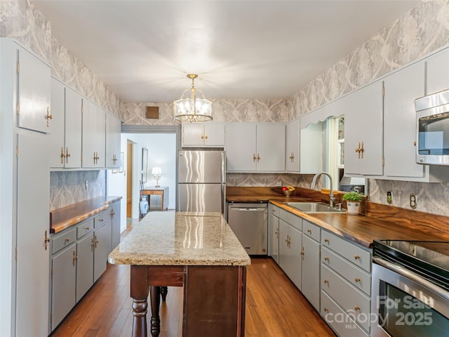 kitchen featuring sink, backsplash, a kitchen island, pendant lighting, and appliances with stainless steel finishes