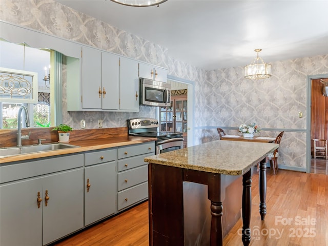 kitchen featuring stainless steel appliances, sink, hanging light fixtures, and light hardwood / wood-style flooring