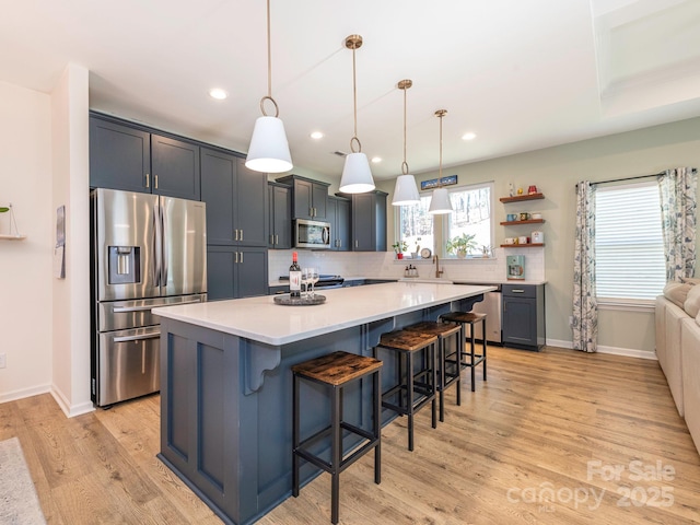 kitchen featuring pendant lighting, appliances with stainless steel finishes, a kitchen island, light wood-type flooring, and a breakfast bar area