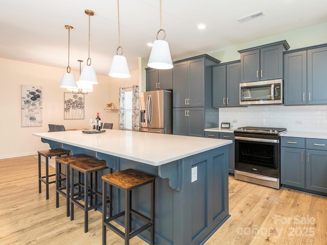 kitchen featuring hanging light fixtures, appliances with stainless steel finishes, a center island, and a breakfast bar area