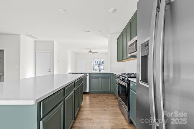 kitchen with kitchen peninsula, green cabinetry, light hardwood / wood-style floors, appliances with stainless steel finishes, and ceiling fan