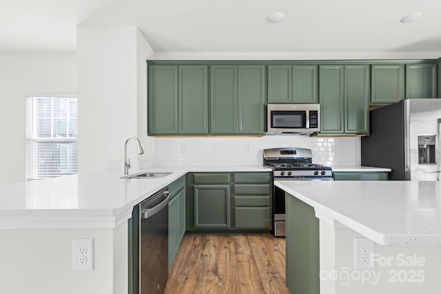 kitchen featuring appliances with stainless steel finishes, kitchen peninsula, light stone counters, decorative backsplash, and sink