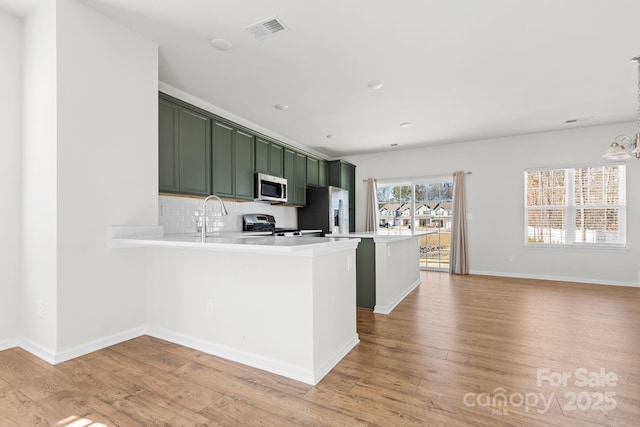 kitchen with kitchen peninsula, green cabinets, stainless steel appliances, light wood-type flooring, and backsplash