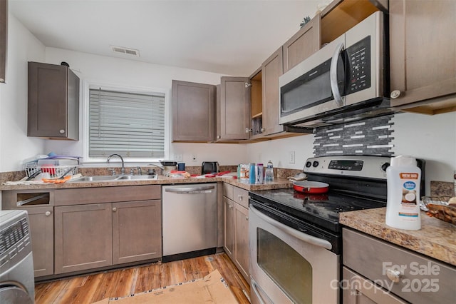 kitchen with appliances with stainless steel finishes, sink, light stone counters, and light hardwood / wood-style flooring