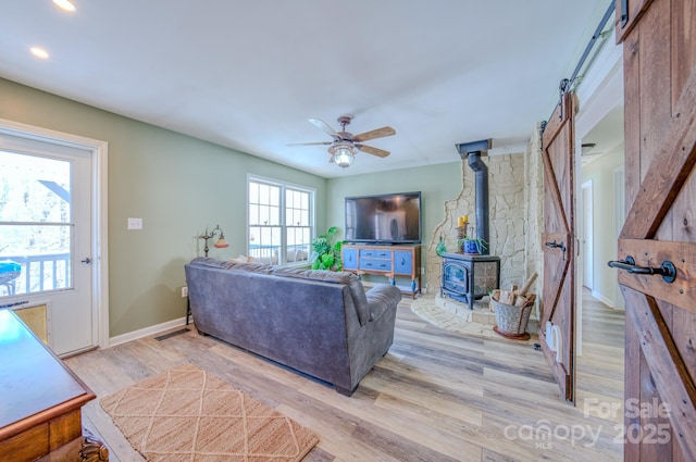 living room with ceiling fan, light wood-type flooring, and a wood stove