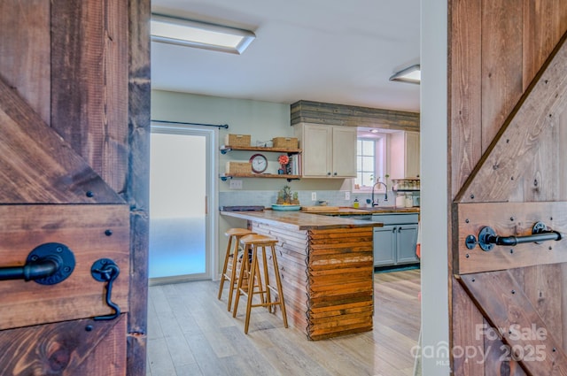 kitchen featuring a breakfast bar, decorative backsplash, light wood-type flooring, wood counters, and sink