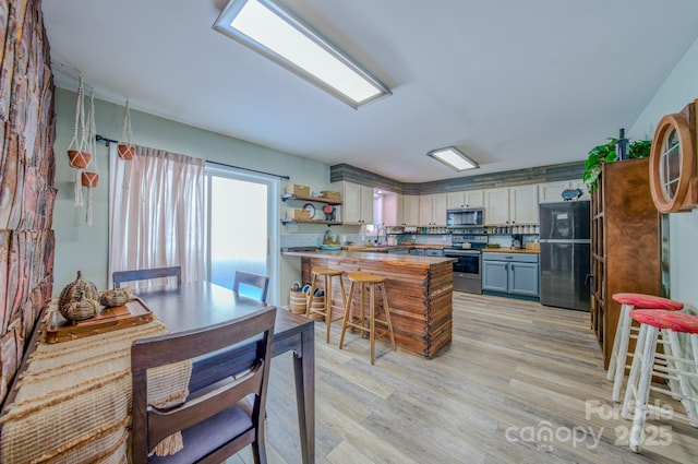 kitchen with light wood-type flooring, gray cabinets, appliances with stainless steel finishes, a kitchen breakfast bar, and sink