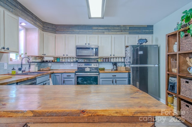 kitchen with stainless steel appliances, butcher block countertops, sink, white cabinets, and tasteful backsplash