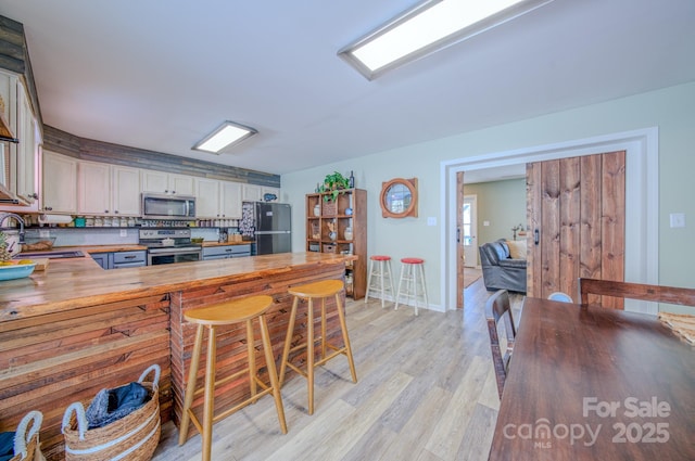 kitchen with stainless steel appliances, tasteful backsplash, light wood-type flooring, butcher block countertops, and sink