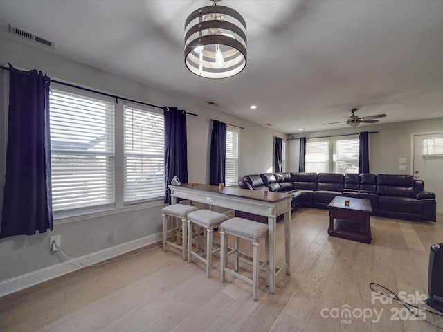 interior space with ceiling fan with notable chandelier, light hardwood / wood-style floors, and a kitchen breakfast bar