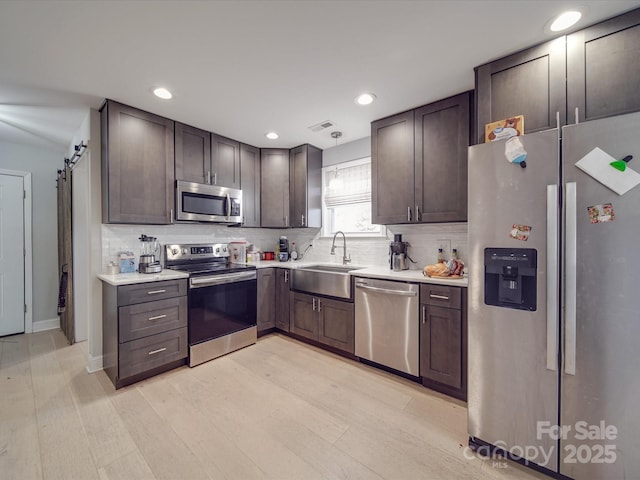 kitchen with stainless steel appliances, a barn door, sink, and dark brown cabinets