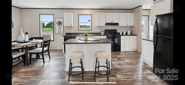 kitchen featuring dark wood-type flooring, white cabinetry, a kitchen bar, a kitchen island, and black appliances