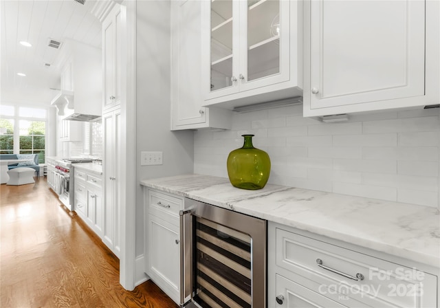 bar featuring white cabinetry, stainless steel range, backsplash, beverage cooler, and light stone countertops