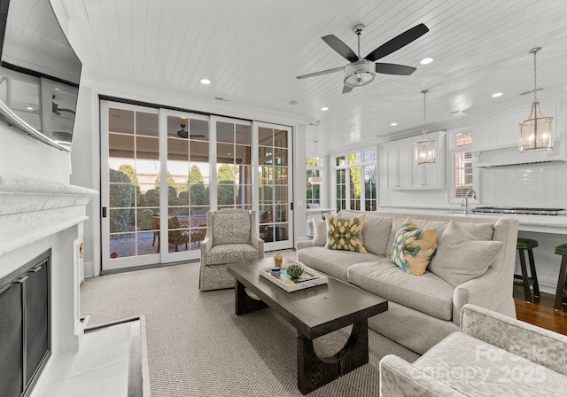 living room featuring ceiling fan, sink, ornamental molding, and wooden ceiling