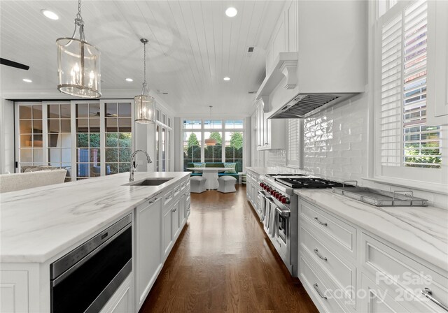 kitchen featuring hanging light fixtures, white cabinets, light stone countertops, and sink