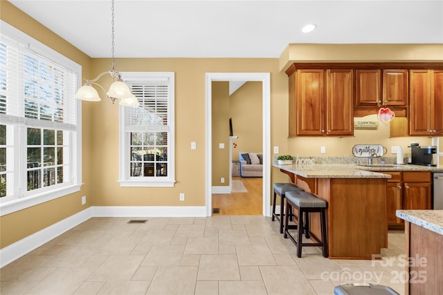 kitchen with sink, stainless steel dishwasher, light stone counters, a kitchen breakfast bar, and pendant lighting