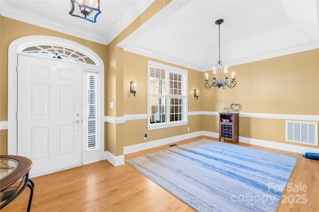 foyer entrance featuring a notable chandelier, ornamental molding, a raised ceiling, and hardwood / wood-style floors