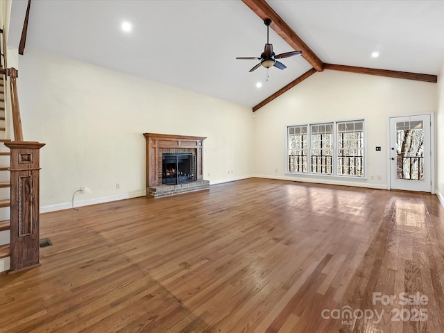 unfurnished living room with ceiling fan, beamed ceiling, a fireplace, and wood finished floors