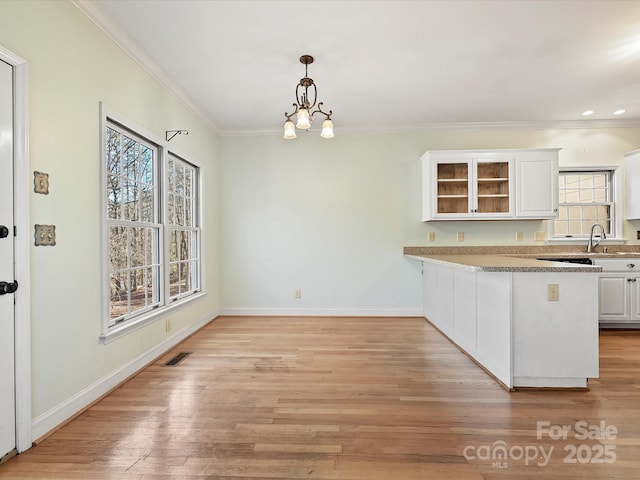 kitchen with a peninsula, visible vents, white cabinets, light countertops, and glass insert cabinets