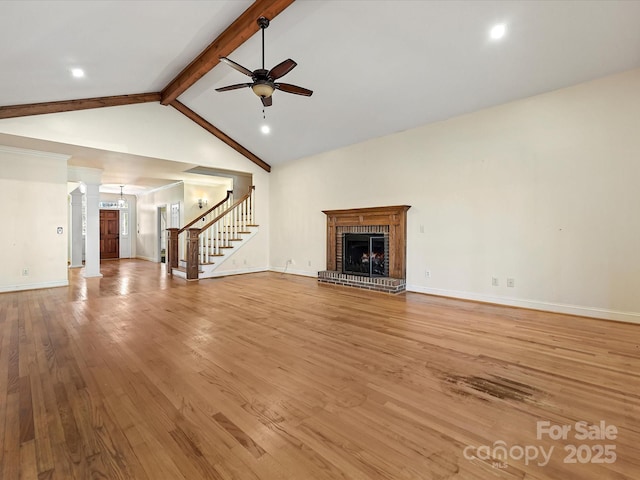 unfurnished living room featuring a ceiling fan, lofted ceiling with beams, light wood-style flooring, stairs, and a fireplace