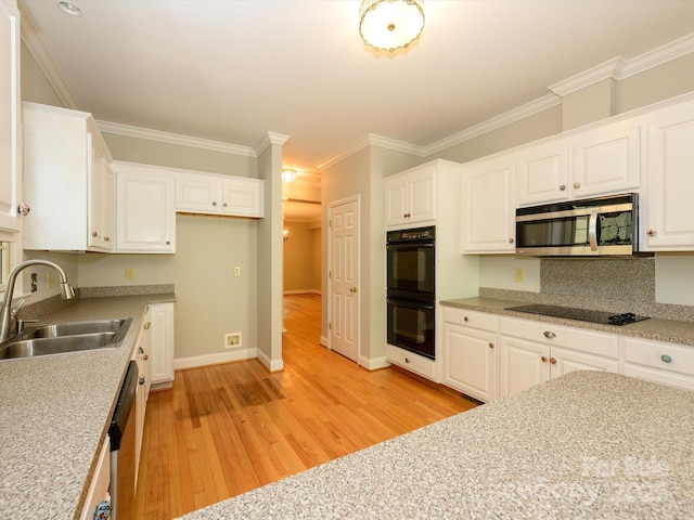 kitchen with white cabinets, a sink, light wood-type flooring, baseboards, and black appliances