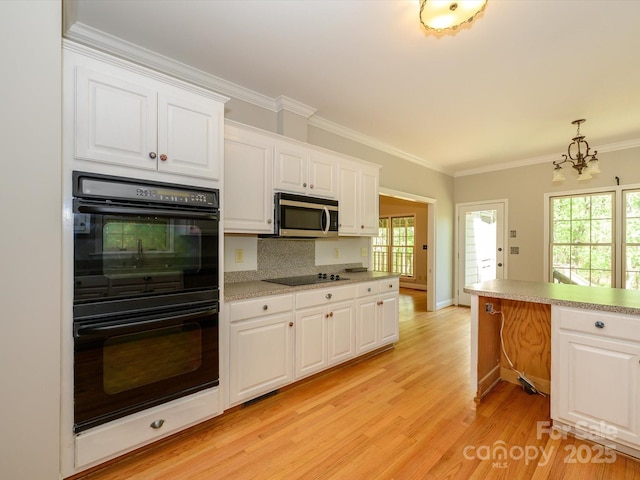 kitchen with black appliances, ornamental molding, a chandelier, and light wood-type flooring