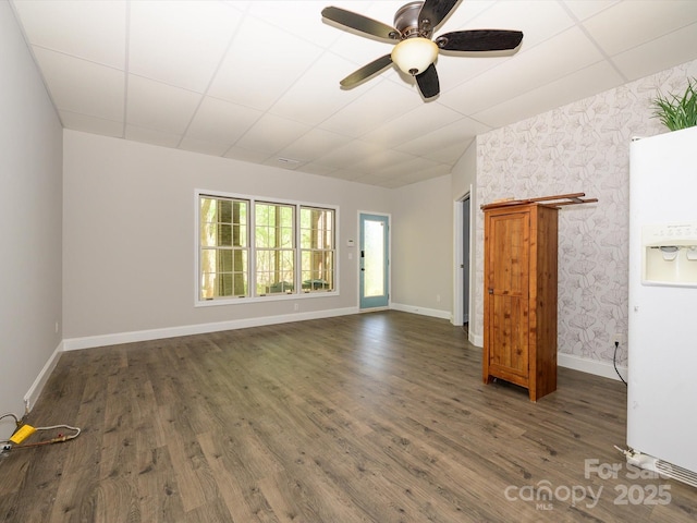 unfurnished living room featuring a drop ceiling, baseboards, wallpapered walls, a ceiling fan, and wood finished floors