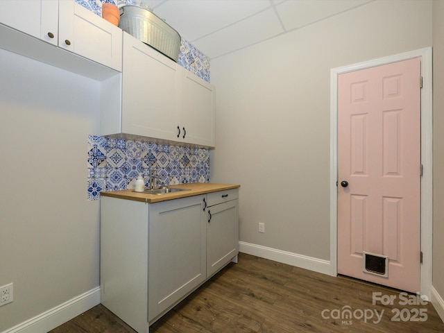 interior space with dark wood-type flooring, butcher block counters, baseboards, decorative backsplash, and white cabinetry