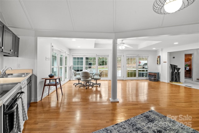 interior space featuring ceiling fan, sink, a raised ceiling, and light wood-type flooring