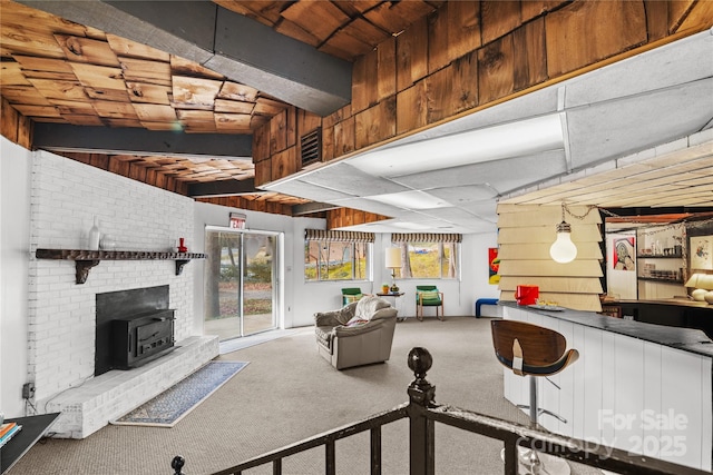 living room featuring carpet, beam ceiling, and a wood stove